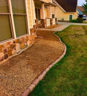 Pea gravel bed with curved paver edging along a stone front home